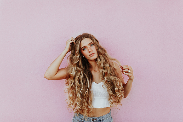 A female posing in front of a pink wall 